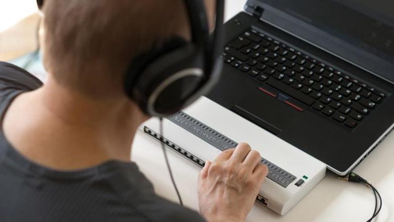 Person using a computer with Braille display and headphones